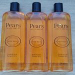 Three bottles of pears body wash on a wooden table.