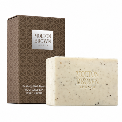 Molton Brown Black Pepper Bodyscrub Soap Bar, 250g, featuring a speckled texture, is displayed in front of its brown patterned packaging labeled "Re-charge Black Pepper.
