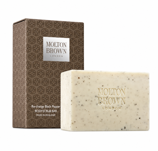 Molton Brown Black Pepper Bodyscrub Soap Bar, 250g, featuring a speckled texture, is displayed in front of its brown patterned packaging labeled "Re-charge Black Pepper.