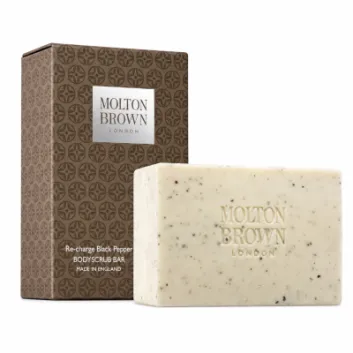 Molton Brown Black Pepper Bodyscrub Soap Bar, 250g, featuring a speckled texture, is displayed in front of its brown patterned packaging labeled "Re-charge Black Pepper.