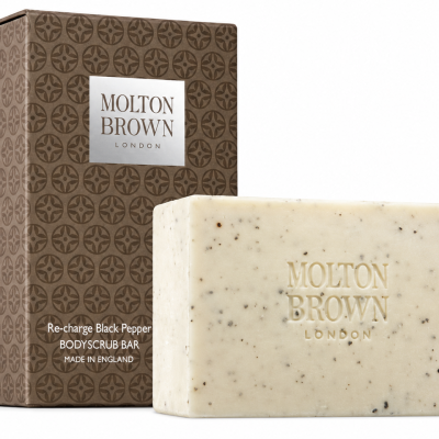 A rectangular Molton Brown Black Pepper Bodyscrub Soap Bar, 250g, sits in front of its brown, patterned box labeled “Re-charge Black Pepper.”.