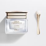 A bottle of Dior Prestige La Creme Exceptional Regenerating & Perfecting Creme next to a spoon.