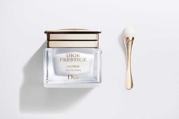 A bottle of Dior Prestige La Creme Exceptional Regenerating & Perfecting Creme next to a spoon.