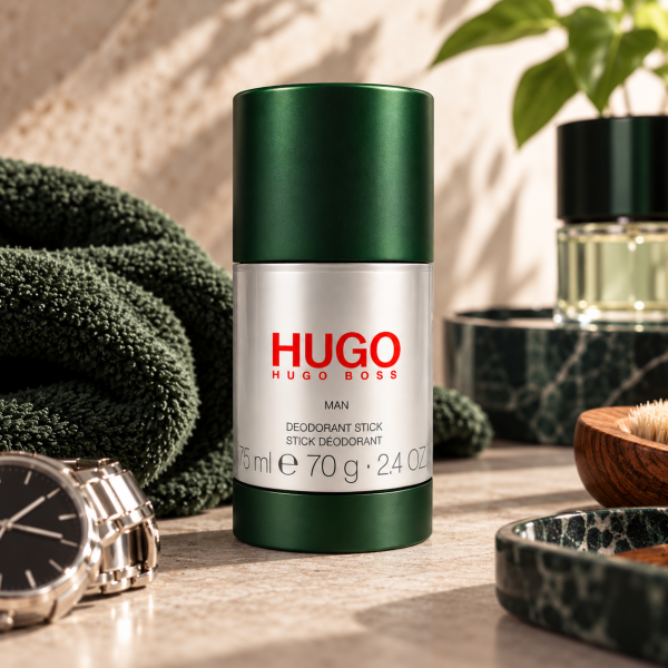 A Hugo Man Deodorant Stick for Men 75ml, Anti-perspirant Spray by Hugo Boss is displayed upright on a bathroom counter alongside a towel, wristwatch, cologne, and a brush.
