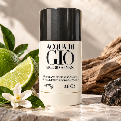 Two Giorgio Armani Acqua di Gio Deodorant Sticks for Men (75ml each) are displayed upright next to a lime, a white flower, leaves, and textured wood in a natural setting.