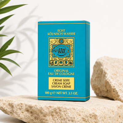 A blue and gold box of Maurer & Wirtz No 4711 Original Cream Soap 100g rests on a stone surface, with rocks and a plant visible in the background.