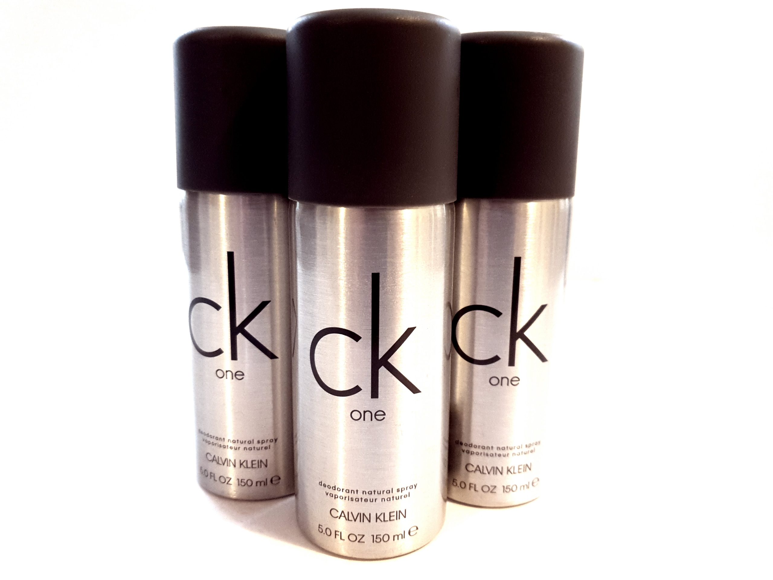 Three bottles of CK One Deodorant Body Spray 150ml on a white background.