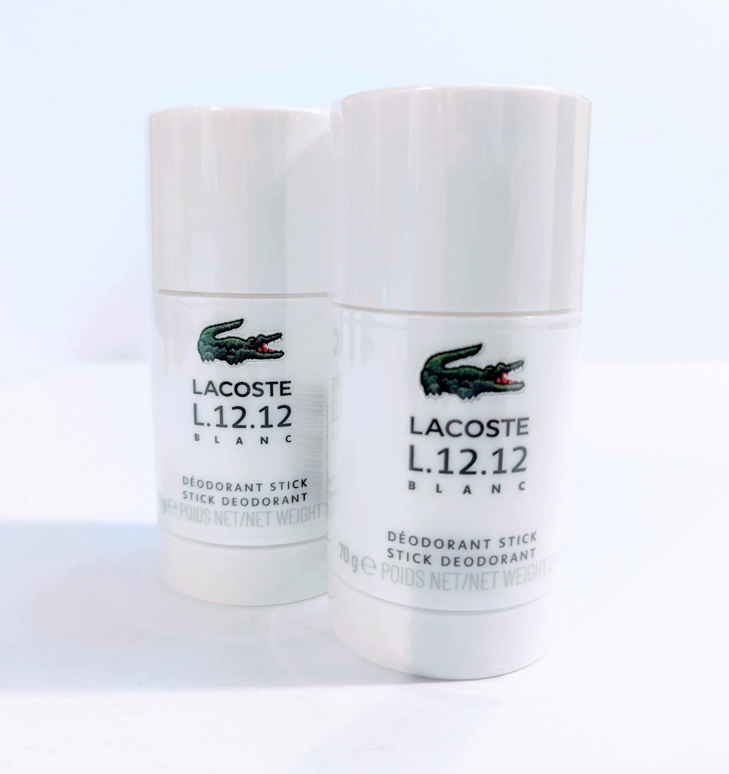 Two Lacoste L.12.12 Blanc Pure Deodorant Stick for Men on a white surface.