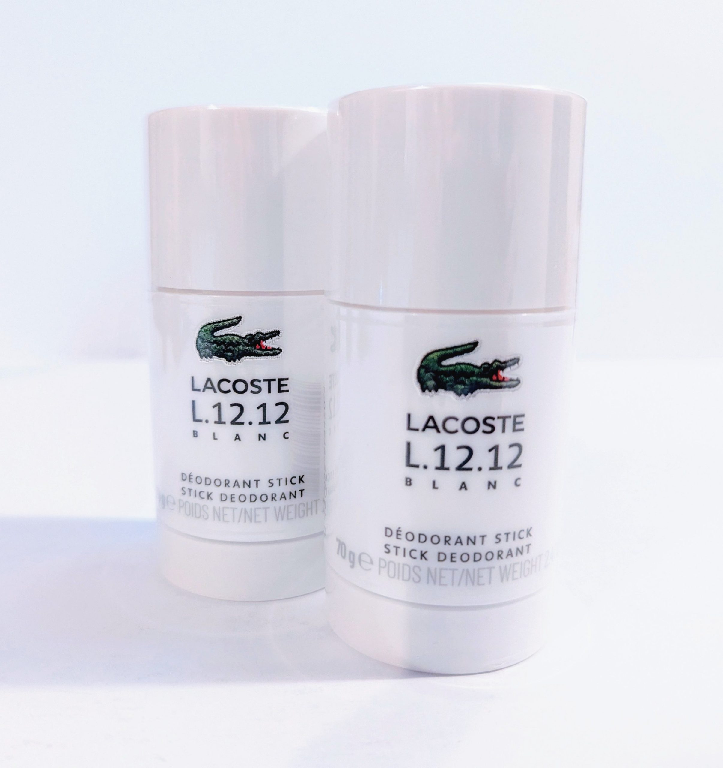 Two Lacoste L.12.12 Blanc Pure Deodorant Sticks on a white surface.