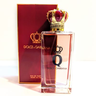 A bottle of dolce & gabbana "the one" perfume with a decorative crown cap beside its box.