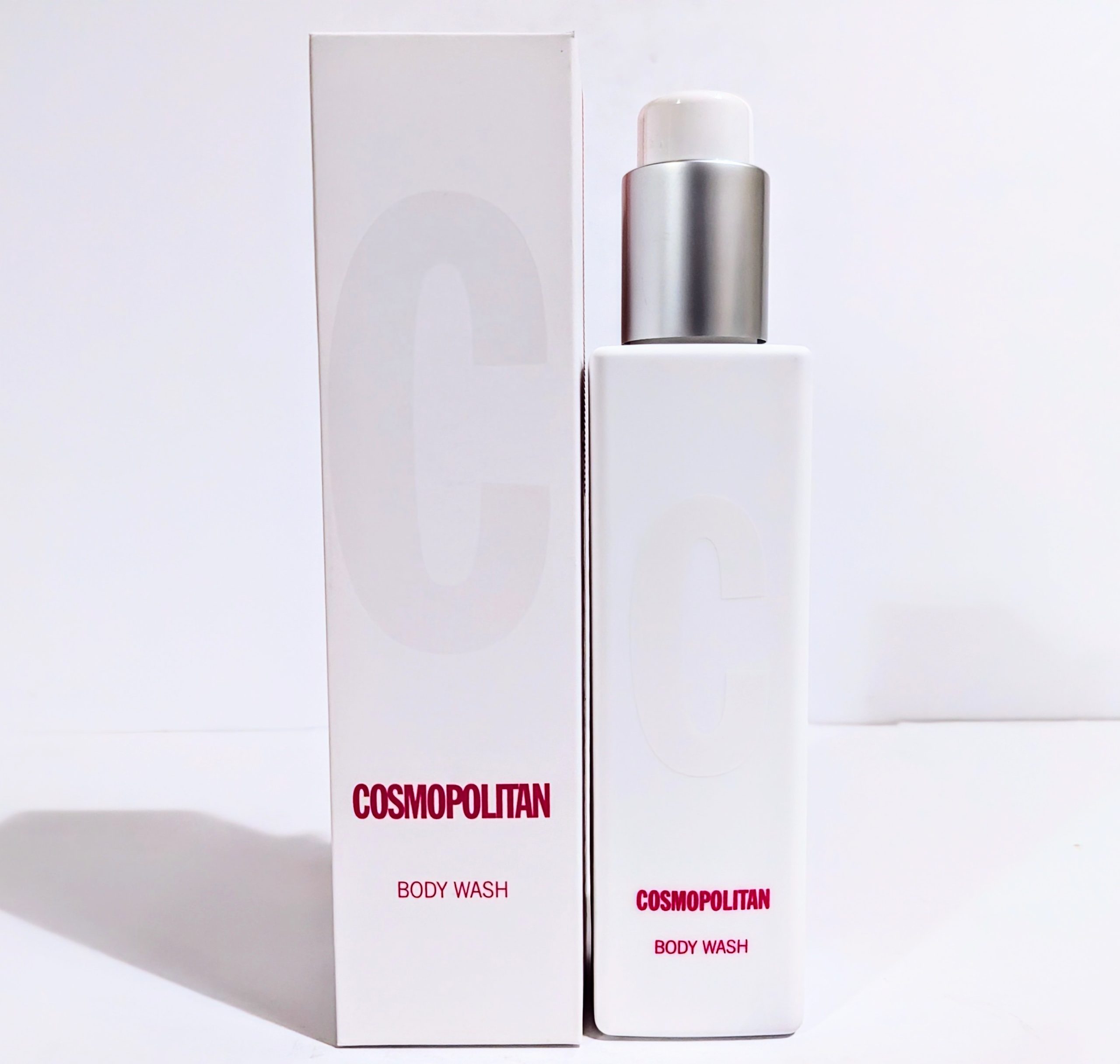 A white bottle of Cosmopolitan body wash with a metallic cap is placed beside its box, which also bears the brand name and logo.