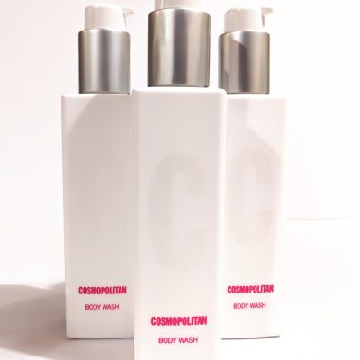 Three white bottles of Cosmopolitan Body Wash with silver pumps are arranged in the image, showing the product label. The bottles feature large embossed "C" letters on the front.