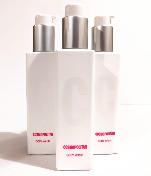 Three white bottles of Cosmopolitan Body Wash with silver pumps are arranged in the image, showing the product label. The bottles feature large embossed "C" letters on the front.