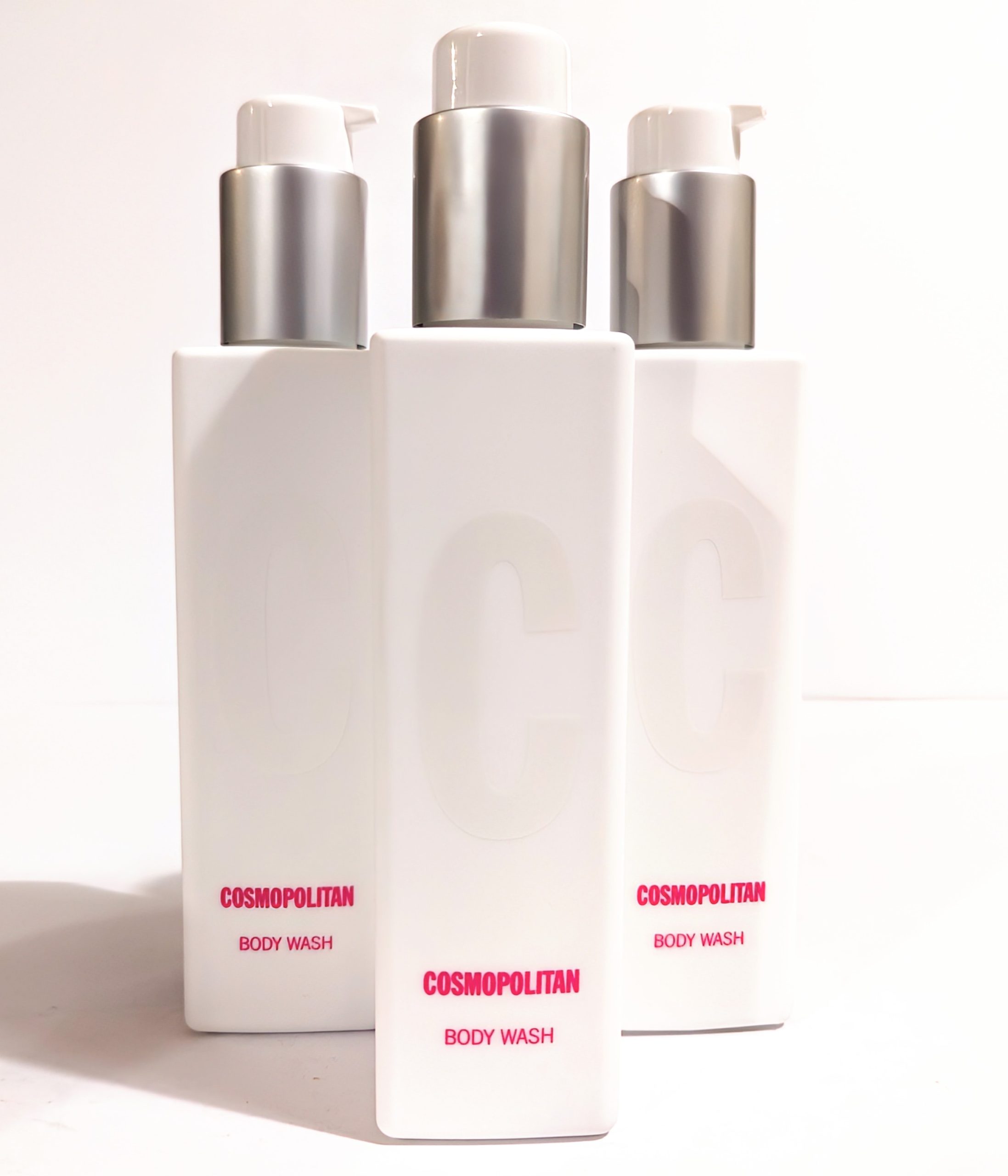 Three white bottles of Cosmopolitan Body Wash with silver pumps are arranged in the image, showing the product label. The bottles feature large embossed “C” letters on the front.
