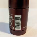 A close-up of the back of a cylindrical deodorant container displaying a barcode, recycling symbols, small text, and the phrase "NET WT 3.0 OZ." The container is metallic brown.