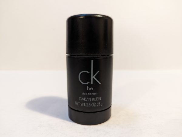 A black, cylindrical deodorant stick with "ck be" written on it in light gray text. The label indicates it is a Calvin Klein product with a net weight of 2.6 ounces (75 grams).
