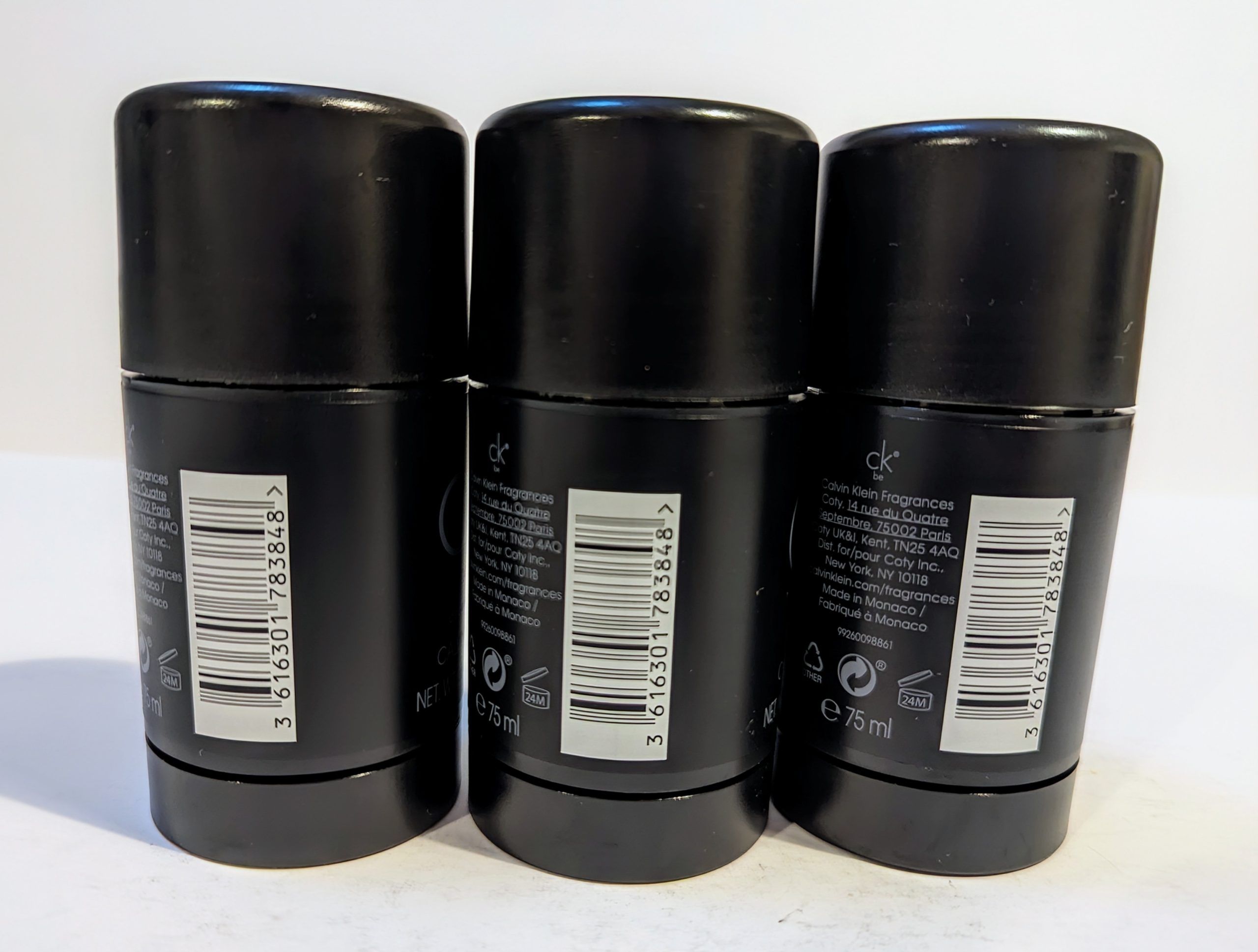 Three black deodorant sticks are arranged in a row, with barcodes and product information visible on the back labels.