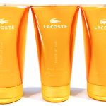 Three orange tubes of Lacoste Touch of Sun Pour Femme body lotion, each with a white Lacoste logo and text.