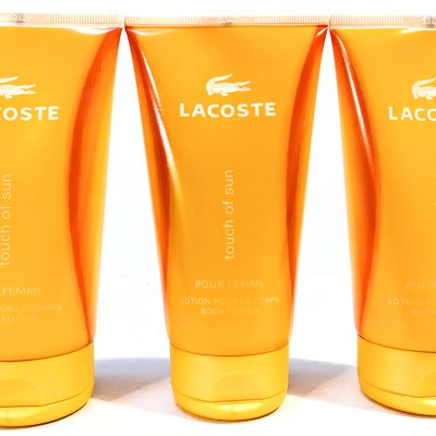 Three orange tubes of Lacoste Touch of Sun Pour Femme body lotion, each with a white Lacoste logo and text.