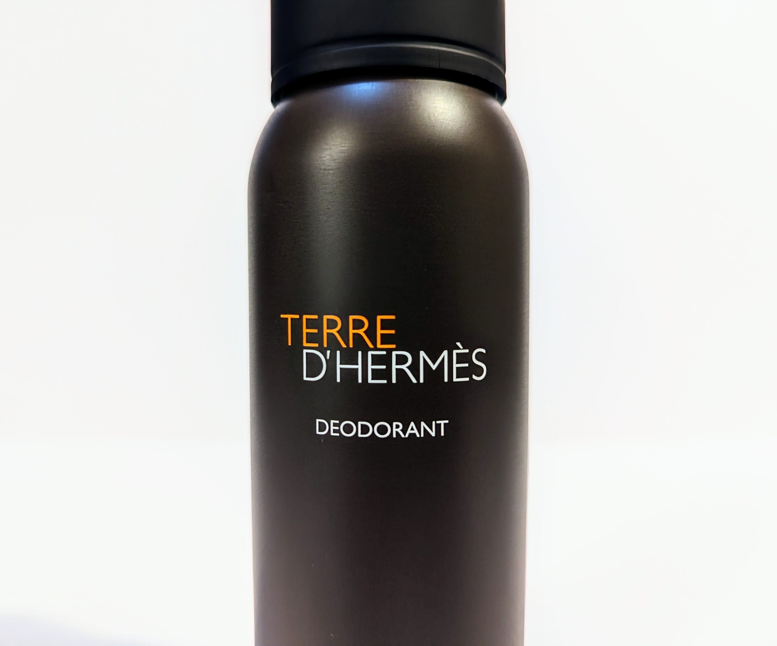 A bottle of Terre d’Hermès deodorant with a black cap and a brown cylindrical body with the brand name printed in orange and white.