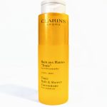 A bottle of Clarins Aroma Tonic Bath and Shower Concentrate with essential oils. The packaging is yellow and tall with white text.