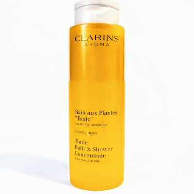 A bottle of Clarins Aroma Tonic Bath and Shower Concentrate with essential oils. The packaging is yellow and tall with white text.