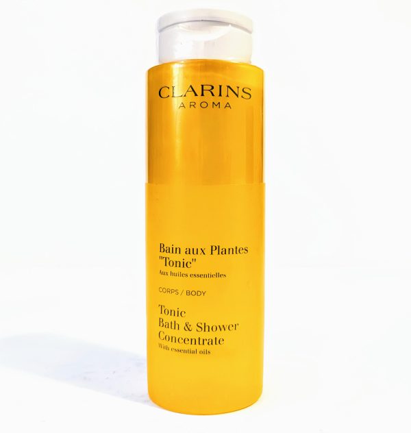 A bottle of Clarins Aroma Tonic Bath and Shower Concentrate with essential oils. The packaging is yellow and tall with white text.