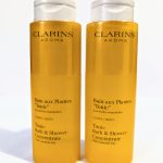 Two yellow bottles of Clarins Aroma Bath and Shower Concentrate with essential oils, labeled "Bain aux Plantes 'Tonic'" for body usage, each with a clear flip-top cap.