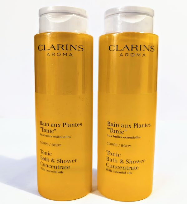 Two yellow bottles of Clarins Aroma Bath and Shower Concentrate with essential oils, labeled "Bain aux Plantes 'Tonic'" for body usage, each with a clear flip-top cap.