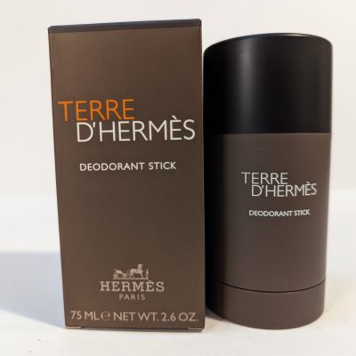 A Terre D'Hermès deodorant stick next to its matching box. The box and the deodorant stick have a brown color scheme with white text. The stick is 75 ml (2.6 oz).