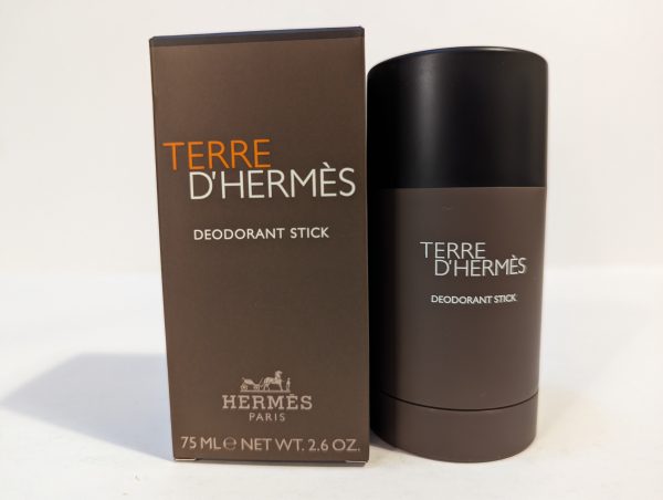 A Terre D'Hermès deodorant stick next to its matching box. The box and the deodorant stick have a brown color scheme with white text. The stick is 75 ml (2.6 oz).