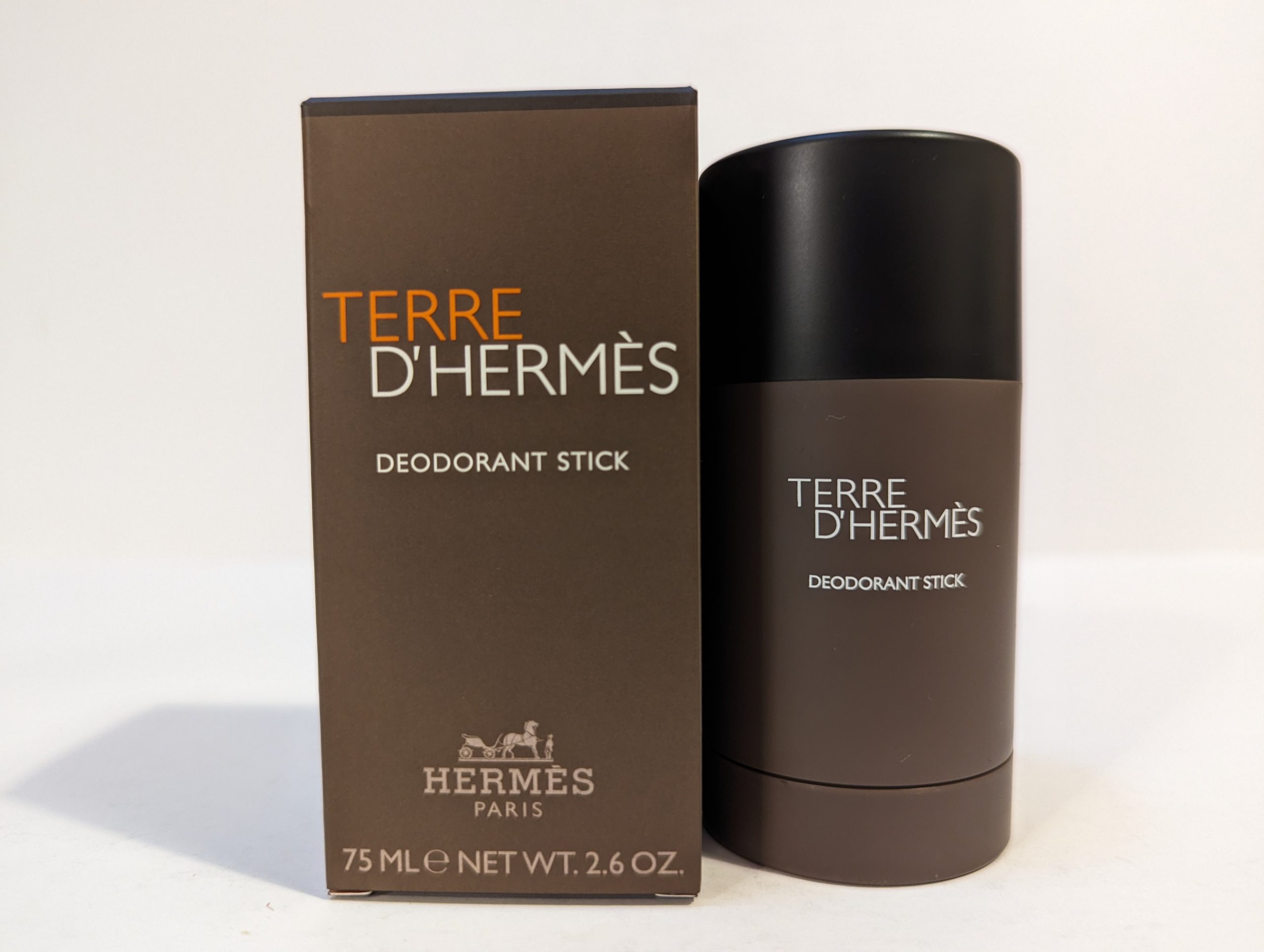 A 75 ml Terre D’Hermès deodorant stick is placed beside its brown packaging box on a plain background.
