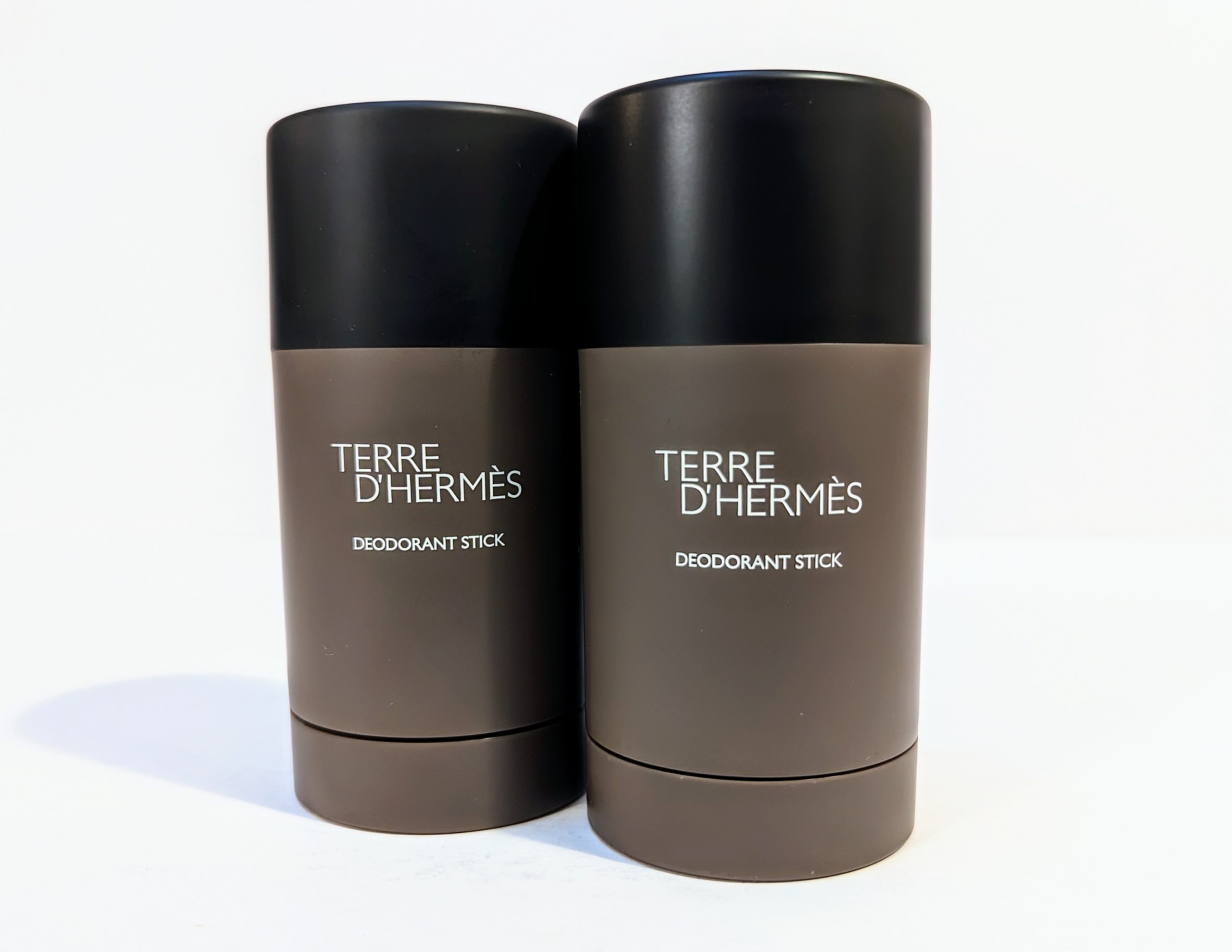 Two bottles of Terre d’Hermès deodorant sticks with brown containers and black caps stand side by side on a white background.