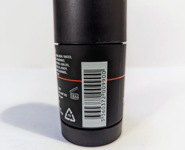 A close-up of a barcode on a cylindrical container with a black label and white text. Recycling symbols and a product longevity icon marked as "18M" are visible below the barcode.