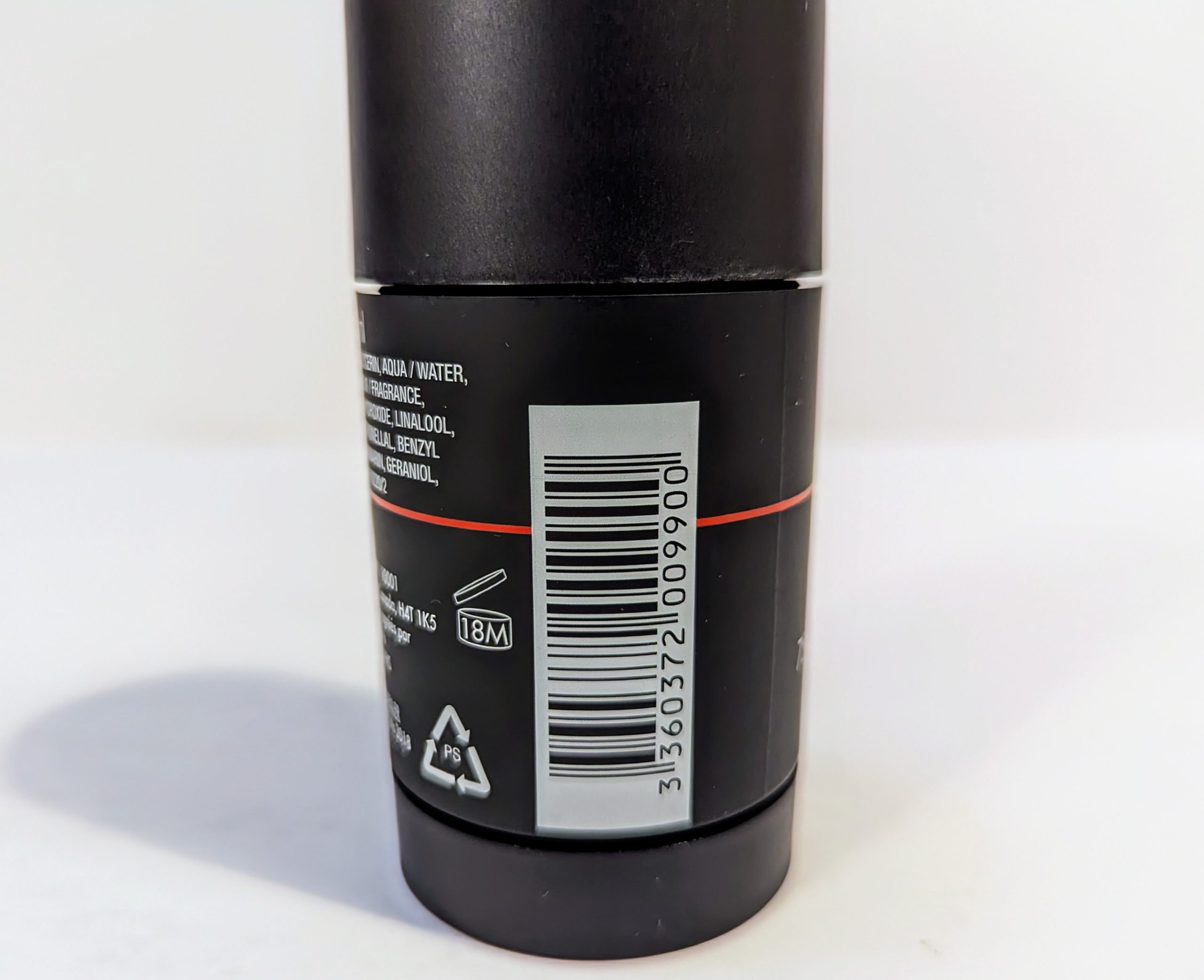 A close-up of a barcode on a cylindrical container with a black label and white text. Recycling symbols and a product longevity icon marked as “18M” are visible below the barcode.