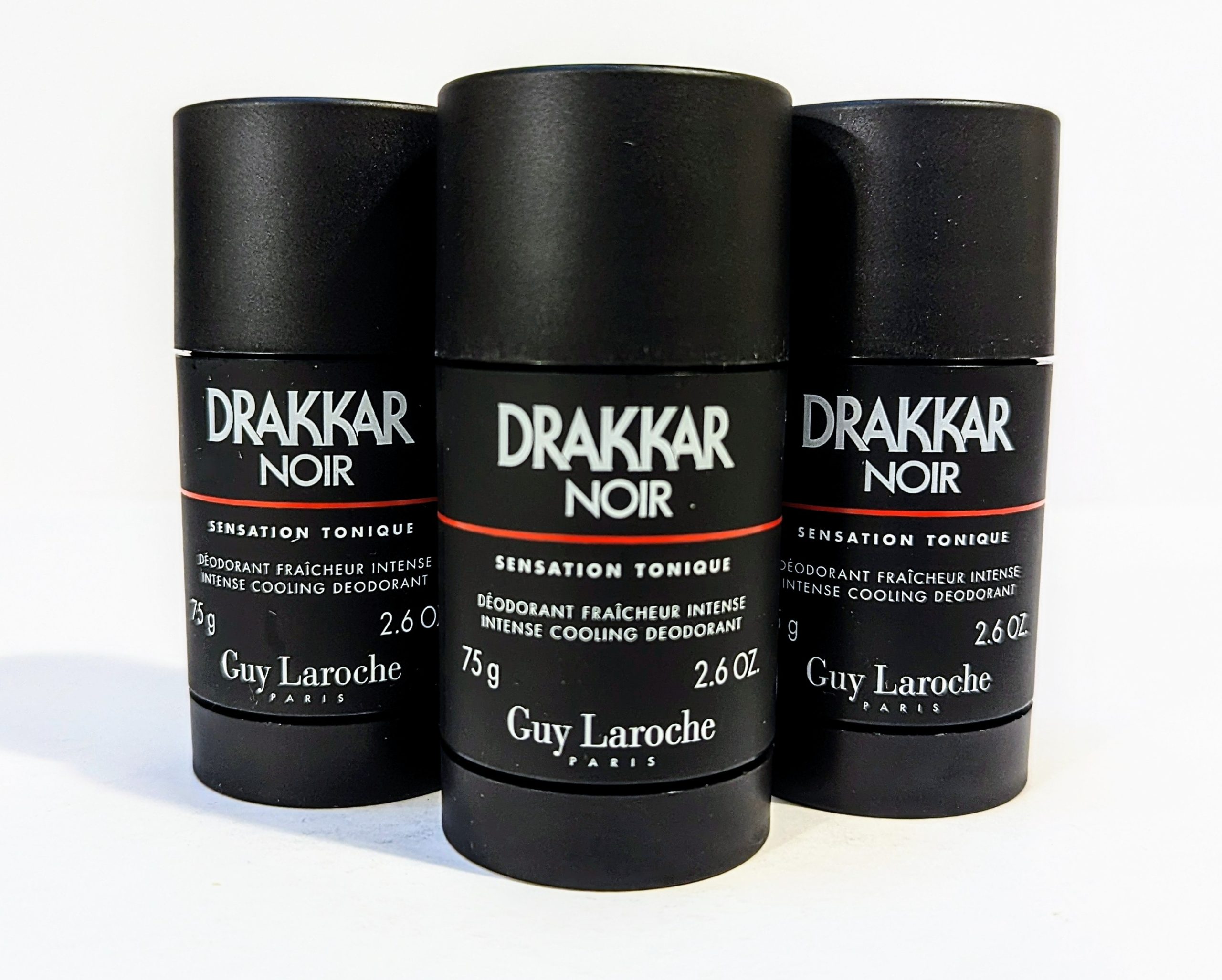 Three black cylindrical deodorant sticks labeled “Drakkar Noir” by Guy Laroche, each with a net weight of 2.6 oz (75 g). They are arranged side by side on a white surface.