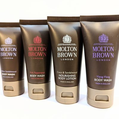 Four tubes of Molton Brown products arranged in a row, including White Sandalwood Body Wash, Pink Pepperpod Body Wash, Coco & Sandalwood Nourishing Body Lotion, and Ylang-Ylang Body Wash.