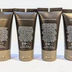 Four black and gray tubes of skincare products with detailed white text on the back, labeled "LONDON VIA MADAGASCAR," "LONDON VIA THE GULF OF GUINEA," "LONDON VIA THE PHILIPPINES," and "LONDON VIA CHINA.