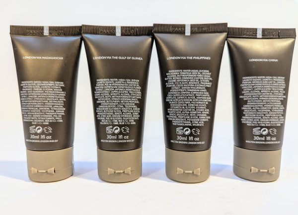 Four black and gray tubes of skincare products with detailed white text on the back, labeled "LONDON VIA MADAGASCAR," "LONDON VIA THE GULF OF GUINEA," "LONDON VIA THE PHILIPPINES," and "LONDON VIA CHINA.