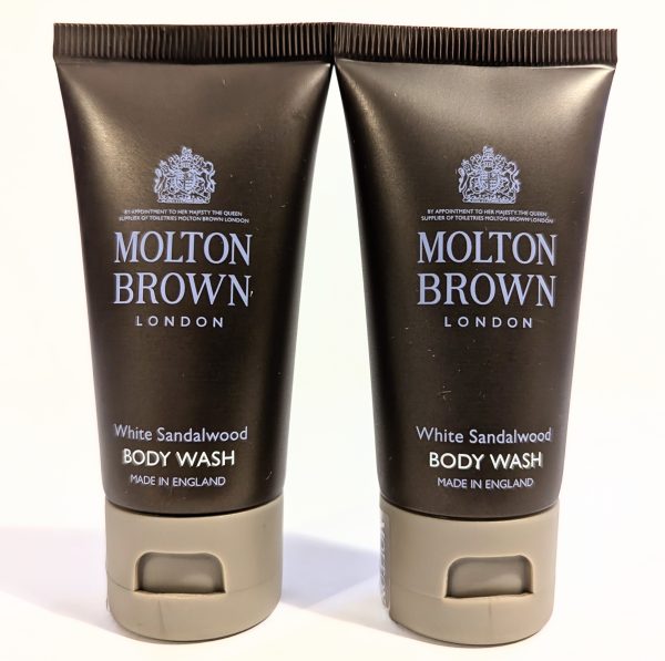 Two black tubes of Molton Brown White Sandalwood Body Wash with silver lettering and beige caps, made in England.