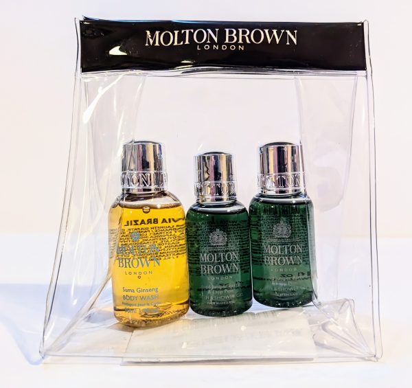 A clear plastic bag containing three Molton Brown London travel-sized bottles: one yellow Suma Ginseng body wash and two green products, likely body lotions or similar items.