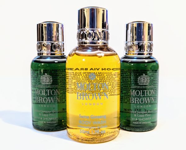 Three Molton Brown bottles: two small, green bottles flanking a larger, yellow bottle. All have mirrored silver caps and detailed labels.