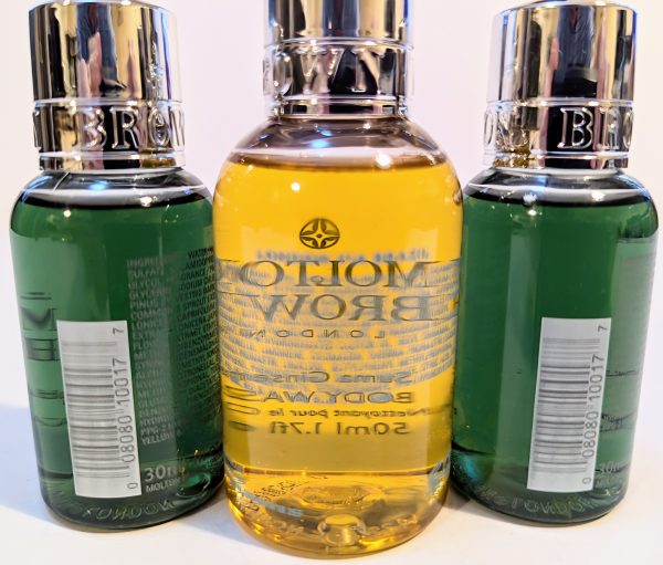 Three Molton Brown bottles with chrome caps; two green bottles flank a central yellow bottle, each displaying barcodes on their back labels.