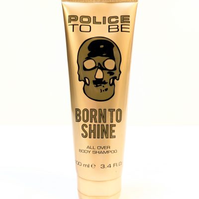 A beige tube labeled "Police To Be Born to Shine All Over Body Shampoo" with a black skull logo. The tube contains 100 ml (3.4 fl. oz.) of product.