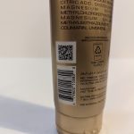 A close-up of the back of a cosmetic tube displaying a QR code, barcode, and product information in multiple languages. The tube is plastic and lists ingredients and recycling information.