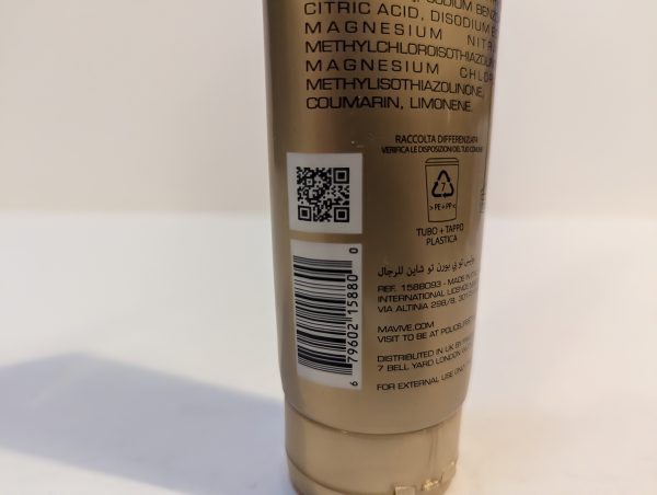 A close-up of the back of a cosmetic tube displaying a QR code, barcode, and product information in multiple languages. The tube is plastic and lists ingredients and recycling information.