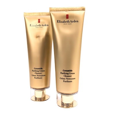Two gold-colored tubes of Elizabeth Arden Ceramide Purifying Cream Cleanser are shown, standing upright. The product name and the brand’s logo are visible on both tubes.