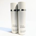 Two white cylindrical cans of L'Eau d'Issey spray deodorant are positioned side by side against a plain background.