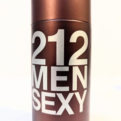 A cylindrical bottle of cologne labeled "212 MEN SEXY" in large white letters on a dark bronze background.