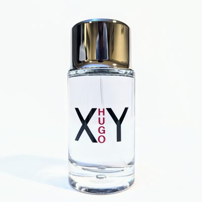 A clear glass bottle of Hugo XY fragrance with a shiny silver cap, filled with colorless liquid, against a plain white background.